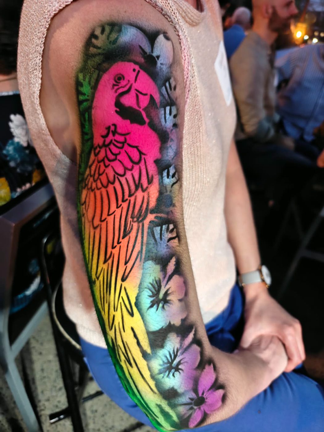 A rainbow parrot airbrushed down a forearm with hibiscus flowers