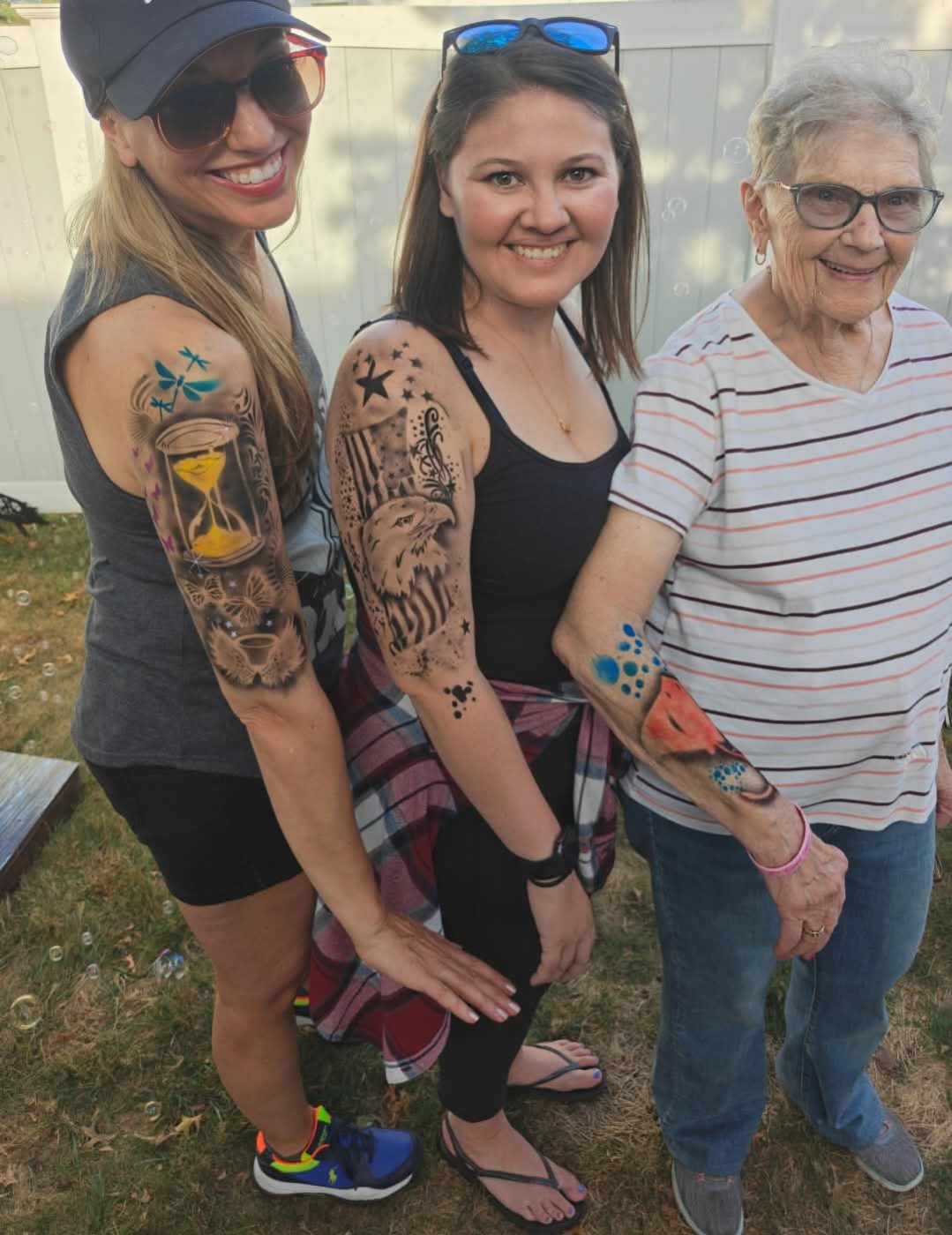 Three guests showing off airbrushed sleeve tattoos at a backyard party