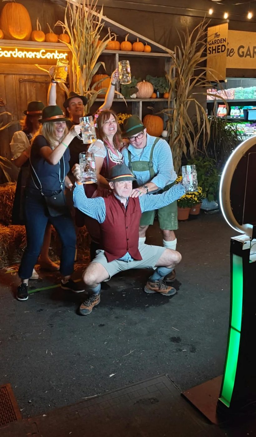 A group posing with beer steins in front of the photo booth at an Oktoberfest event
