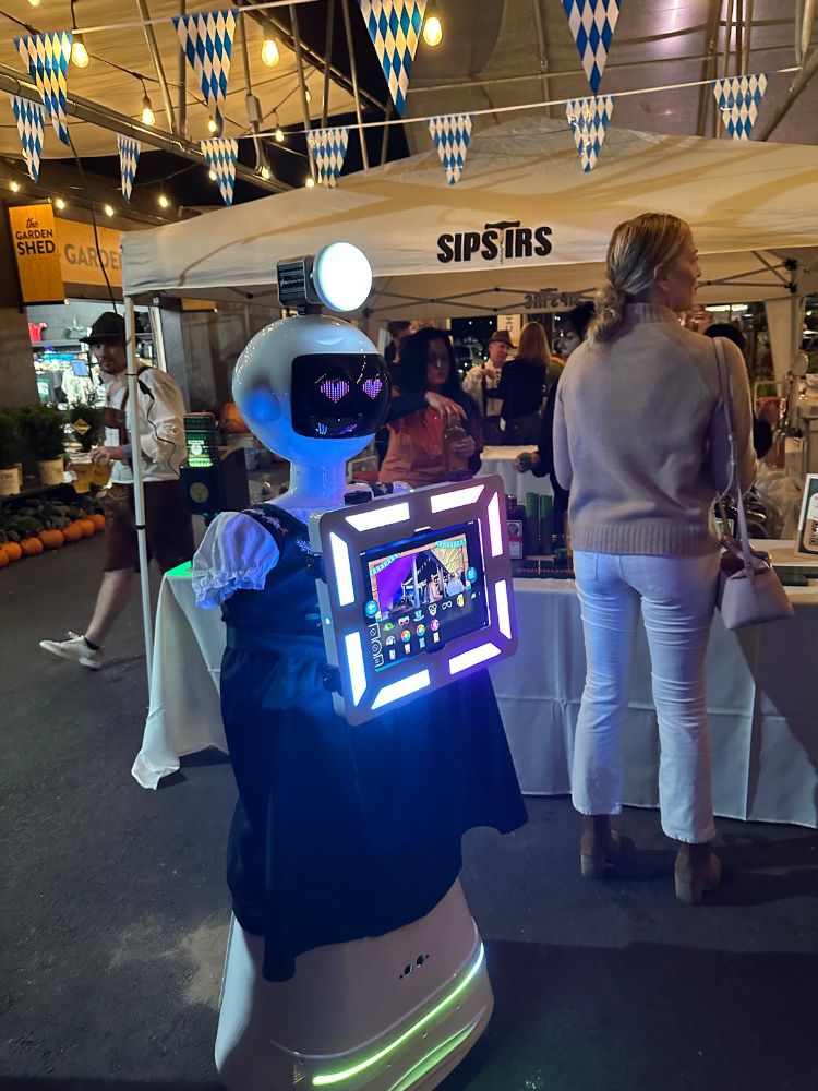 The robot photo booth dressed in a dirndl with heart eyes and a lit touchscreen at an Oktoberfest