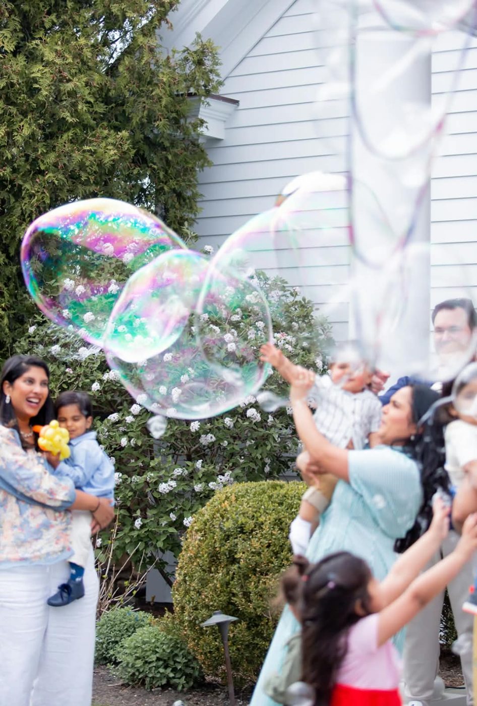 Guests reaching up to catch giant iridescent bubbles at an outdoor party