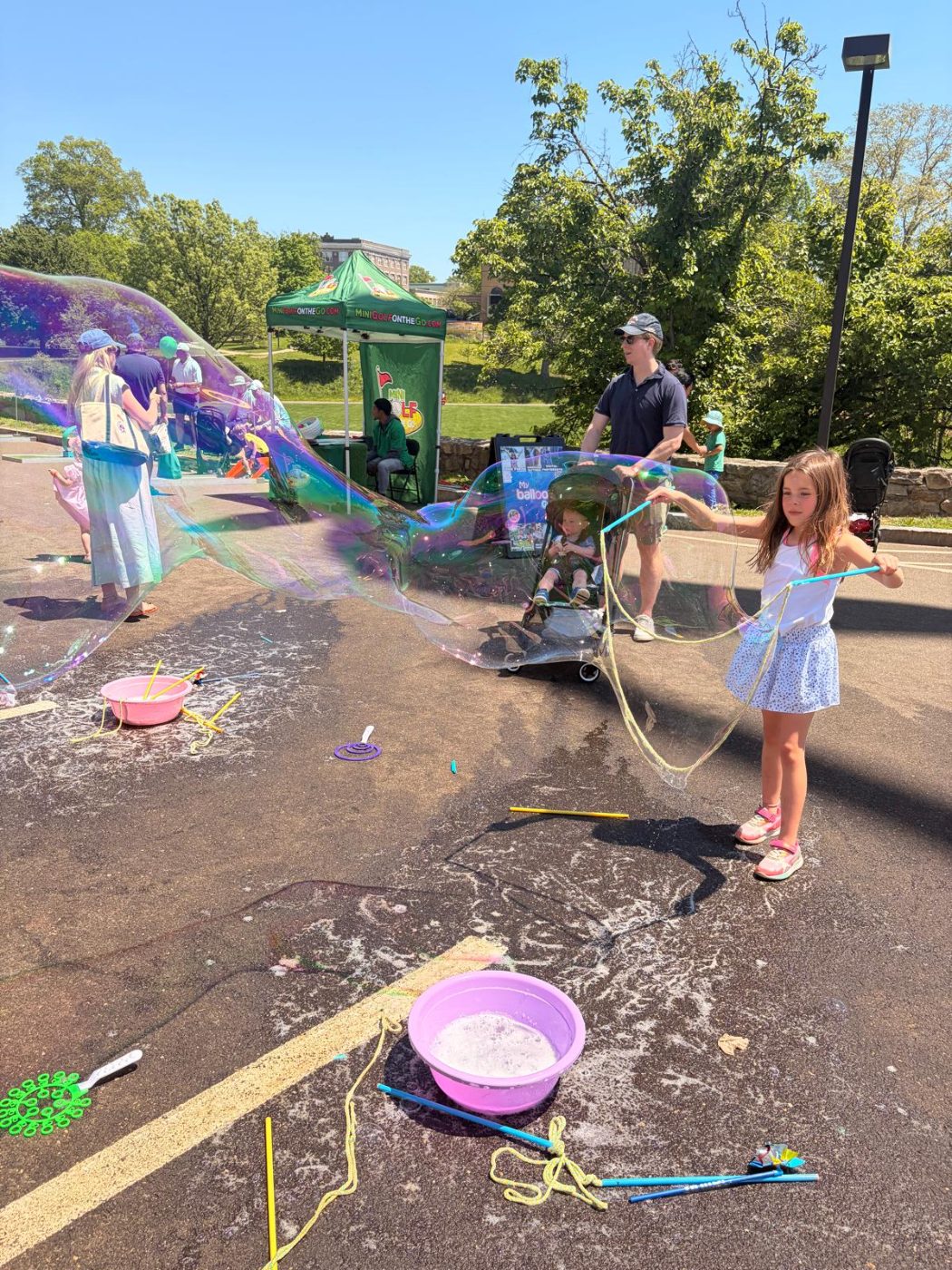 A girl pulling a giant bubble out of a tray with a rope wand