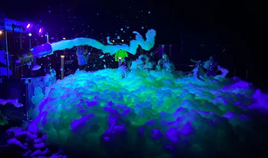 A glowing mountain of foam lit up green and purple at a night foam party
