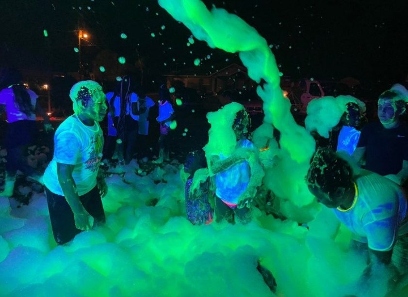Kids covered in glowing green foam under blacklight at a glow foam party