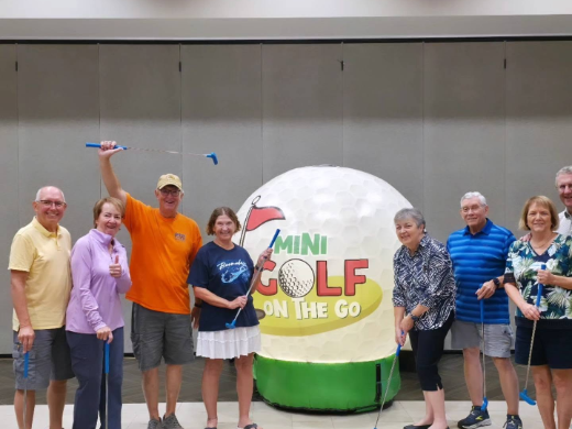 Adults posing with the giant inflatable golf ball at an indoor mini golf event
