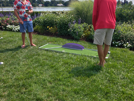 Two adults playing a mini golf hole on a waterfront garden lawn