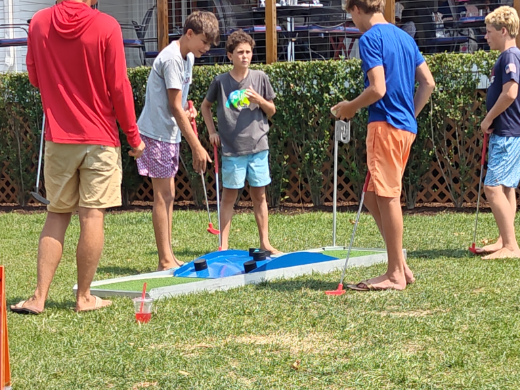Teens playing the blue bumper obstacle hole at a backyard party