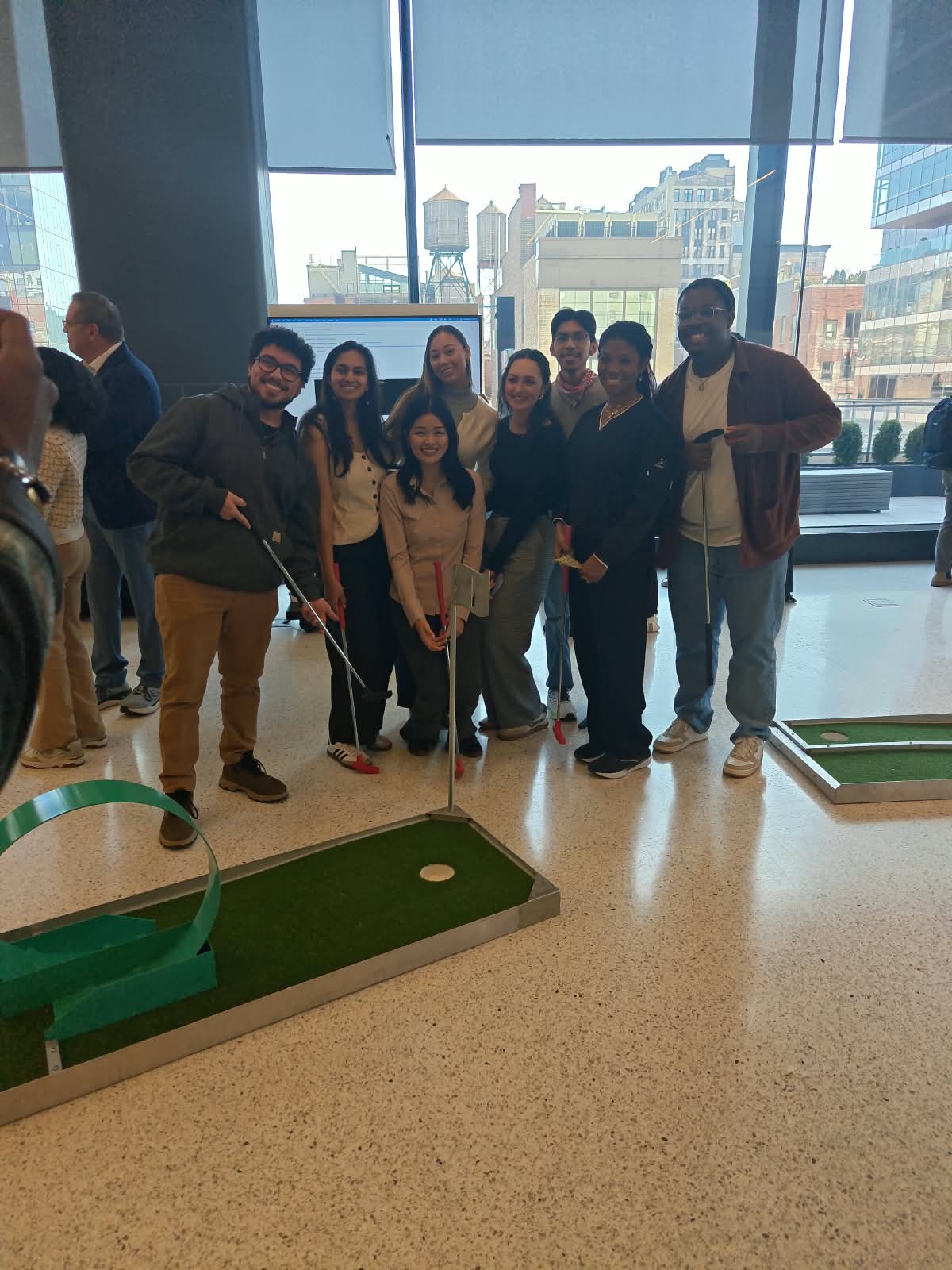 A team of coworkers posing with putters around an indoor mini golf hole at a city office event