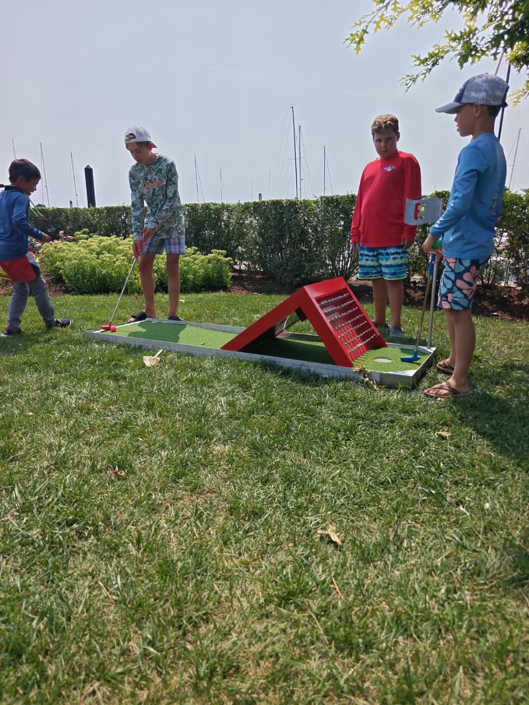 Kids lining up a putt on a red ramp hole with the marina behind them