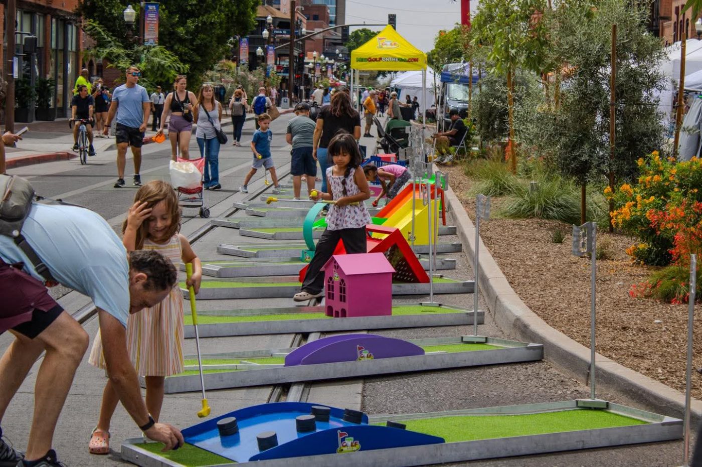 A nine-hole mini golf course set up down a closed downtown street at a festival