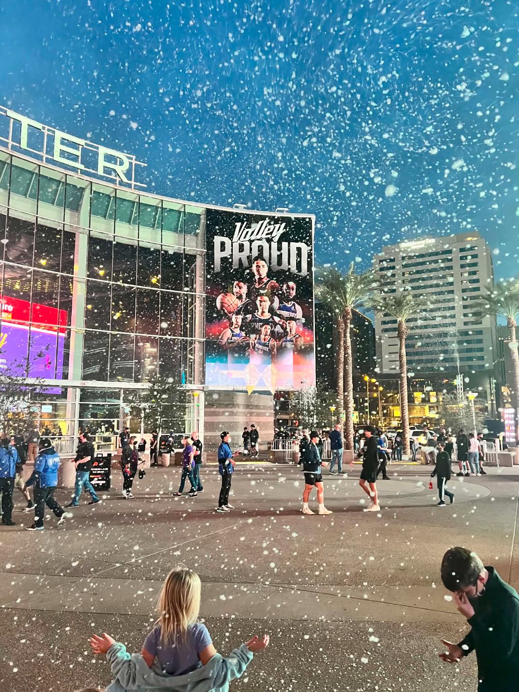 Snow falling over an arena plaza as fans arrive for a game