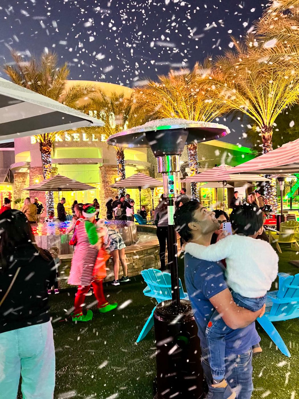Snow falling over palm trees and a courtyard crowd at a holiday event