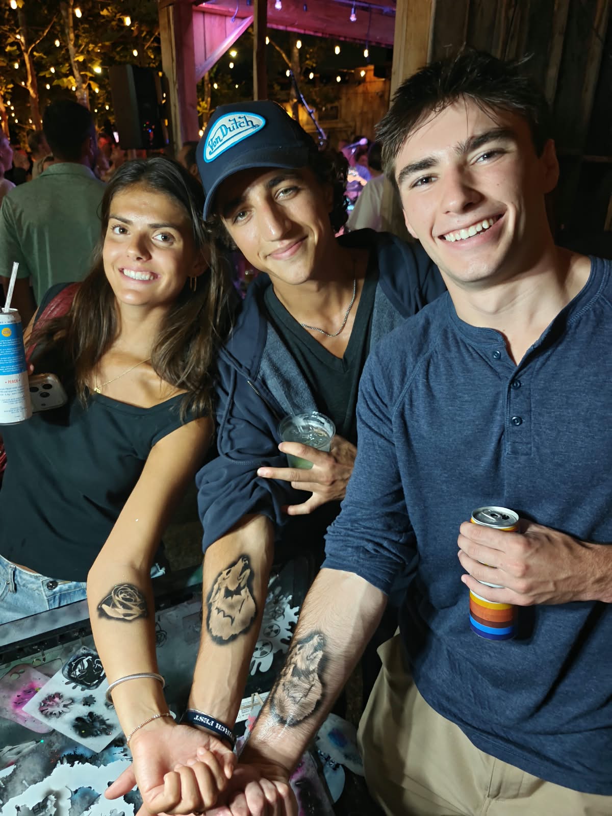 Three friends showing off airbrush tattoos at an evening event