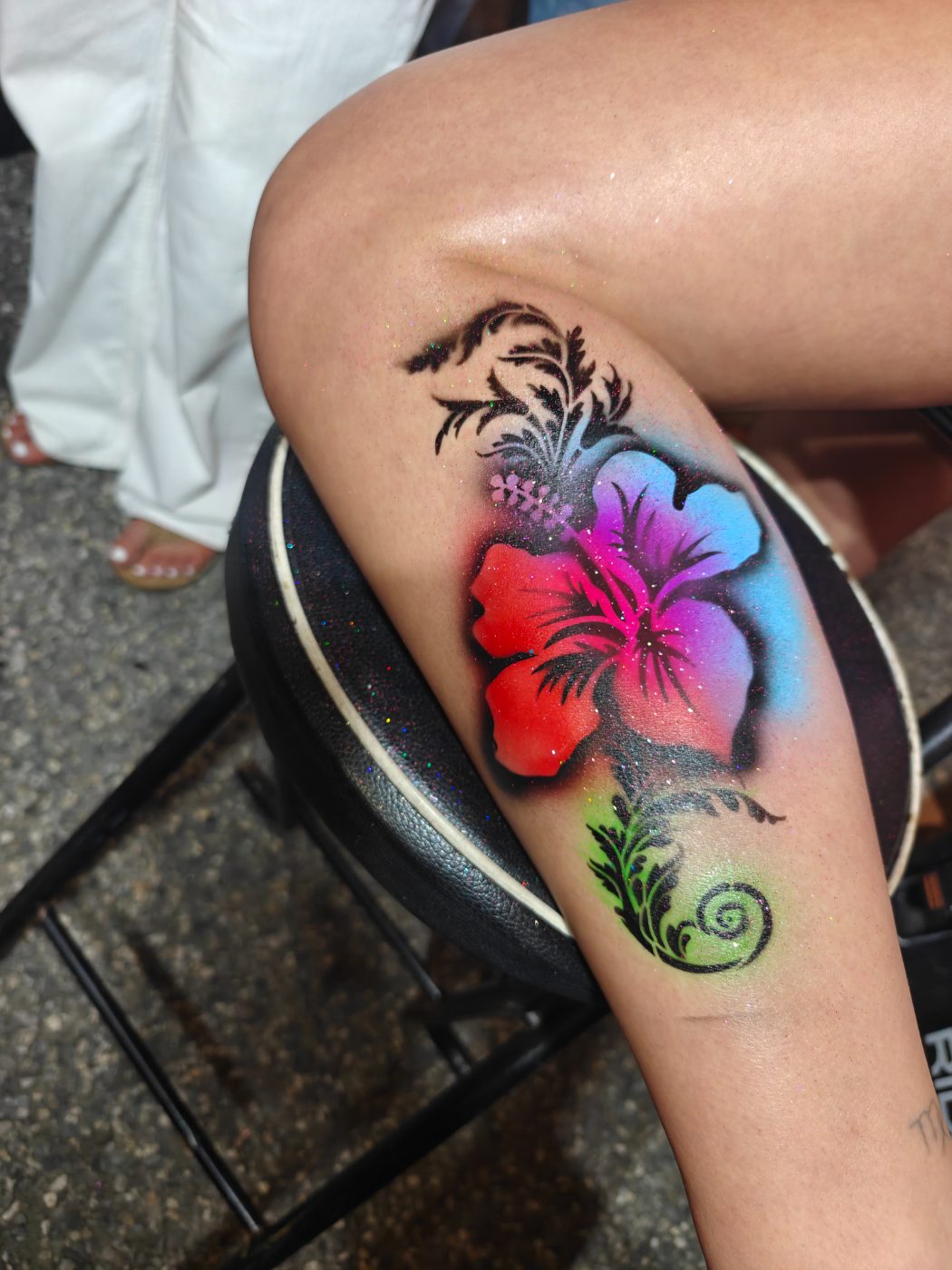 Airbrushed hibiscus flower on a leg in red, pink and blue with glitter