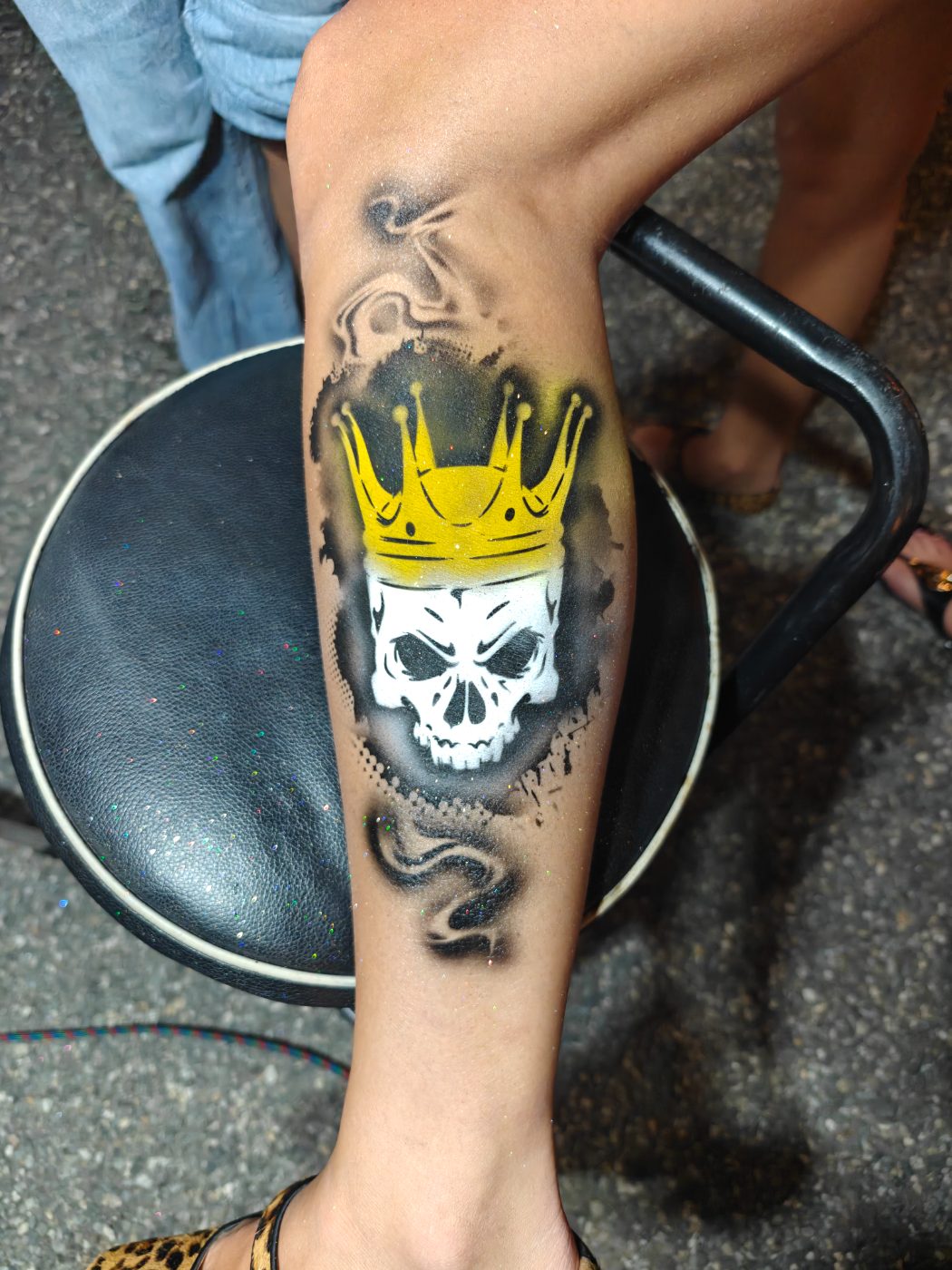 Airbrushed skull wearing a gold crown, sprayed on a calf