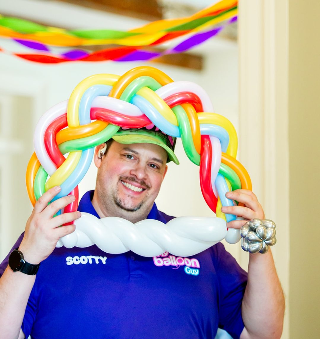 Scotty holding up a woven rainbow balloon arch